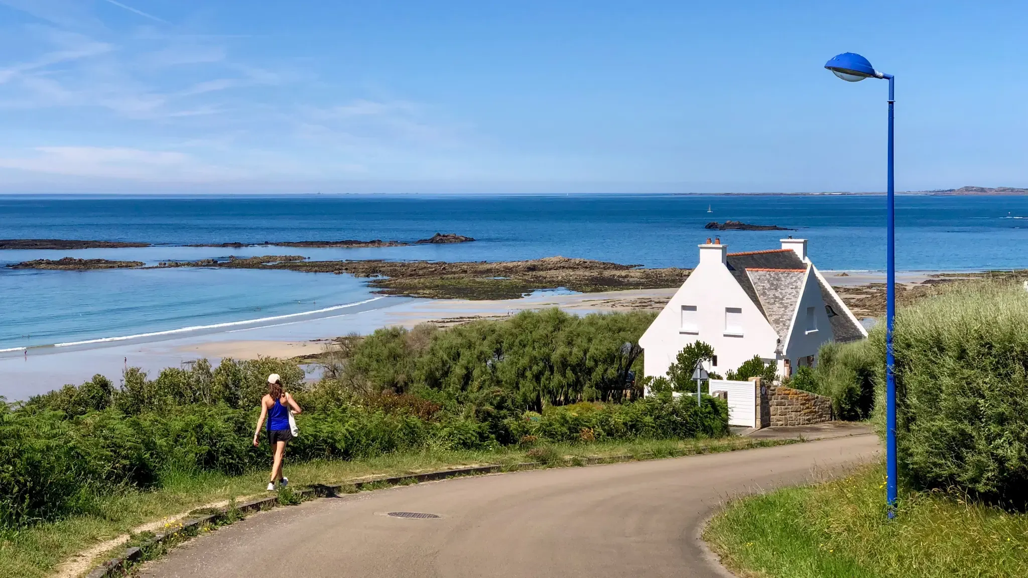 A sunny day on the Britanny coast with a small white house and calm sea in the background.
