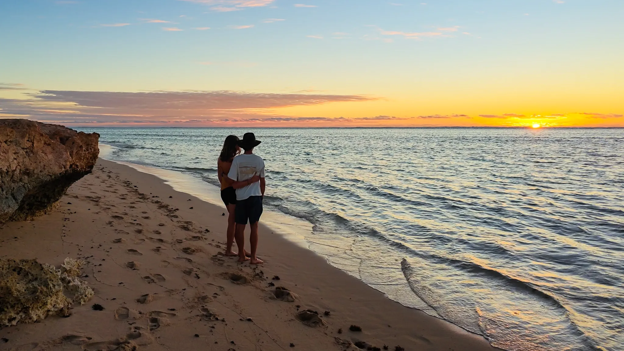 Guillaume and Mylene standing on the beach, watching the sunset