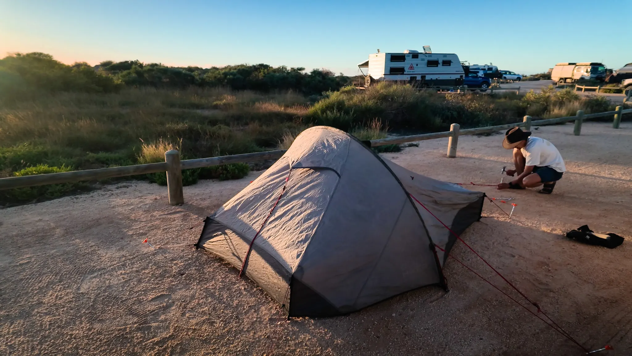 Guillaume pitching a small tent in the campground at sunset.