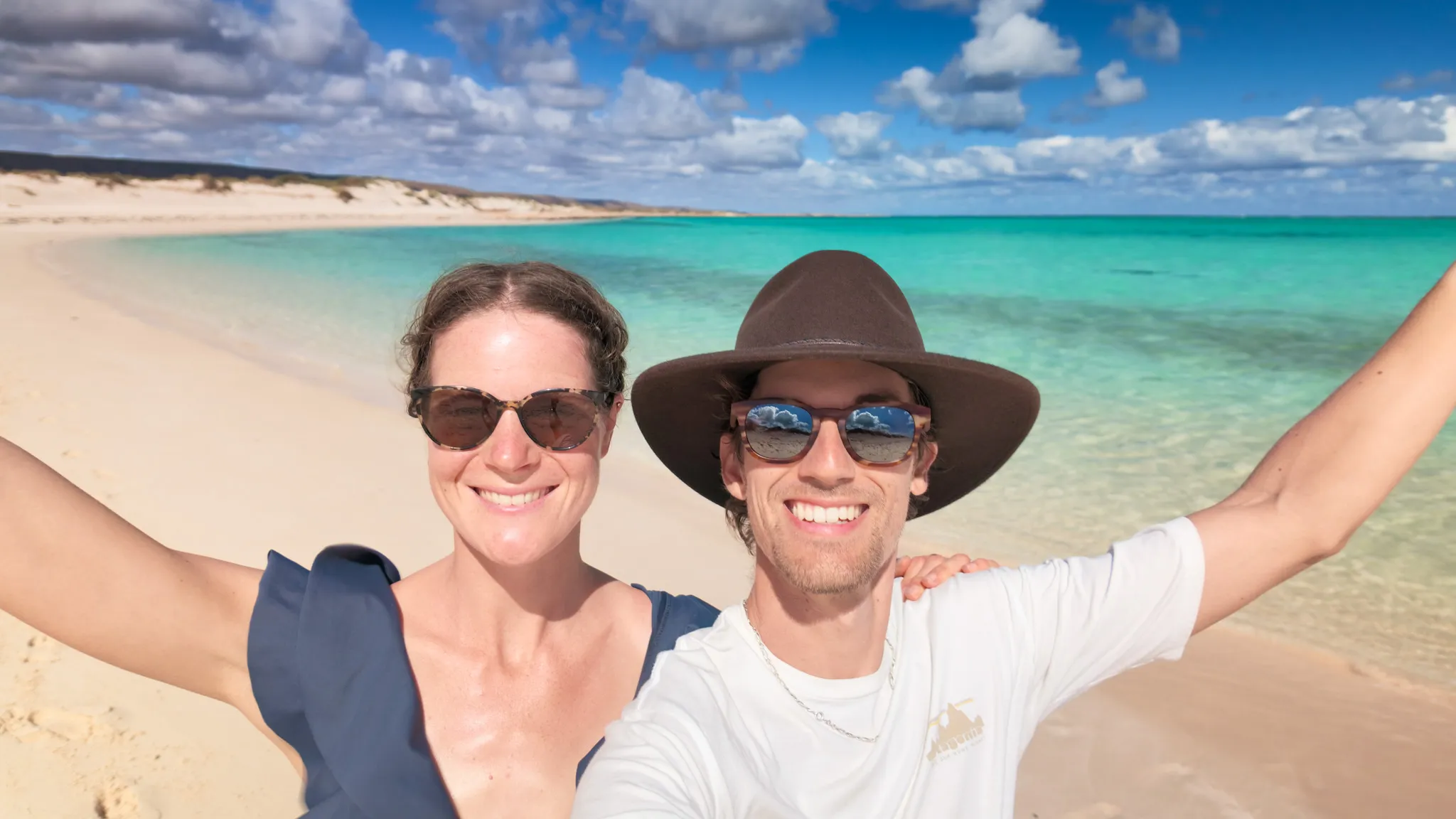 Mylène and Guillaume standing on the dunes, overlooking the turquoise bay.